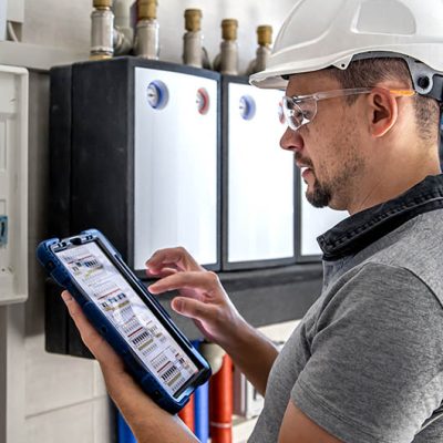 Man, an electrical technician working in a switchboard with fuses. Installation and connection of electrical equipment. Professional uses a tablet.
